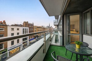 A balcony with a glass table and chairs, a small potted plant, and a view of the cityscape. - Super Deluxe Two-bedroom Apartment (London)