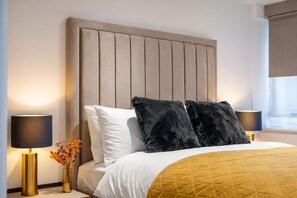 A hotel room with a large bed, two bedside lamps, a vase with flowers, and a window with curtains. - Super Deluxe Two-bedroom Apartment (London)