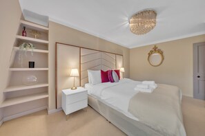 A bedroom with a bed, bedside tables, a nightstand, a chandelier, a mirror, and a door. - Deluxe-2bedroom Apartment Behind Harrods w AC (London)