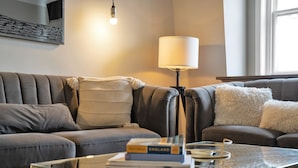 Ett modernt vardagsrum med en soffa i läder, ett soffbord i glas med böcker, en lampa och en inramad tavla på väggen.
