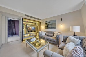 A modern living room with a glass coffee table, grey sofas, a flat-screen TV, and ambient lighting. - Deluxe-2bedroom Apartment Behind Harrods w AC (London)
