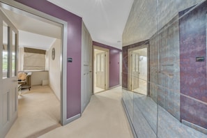 A hallway with a carpeted floor, doors, and a wall with a textured surface. - Deluxe-2bedroom Apartment Behind Harrods w AC (London)