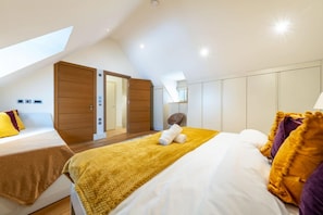 Ein Schlafzimmer mit schrägen Wänden, einem Bett mit gelber Decke, einem Holzschrank und einem kleinen runden Tisch.