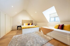 Ein Schlafzimmer mit schrägen Wänden, einem Bett mit gelb-lila Bettwäsche, einem weißen Sofa und einem kleinen Tisch mit einer Lampe.