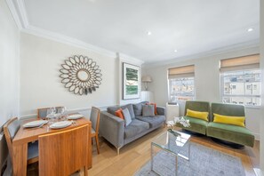 A modern living room with a dining area, a grey sofa, and a green sofa with yellow cushions. - Deluxe 2 Bedroom Apartment (London)