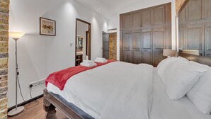 Una habitación de hotel con una cama grande, una pared de ladrillo, un armario de madera y una lámpara de pie.