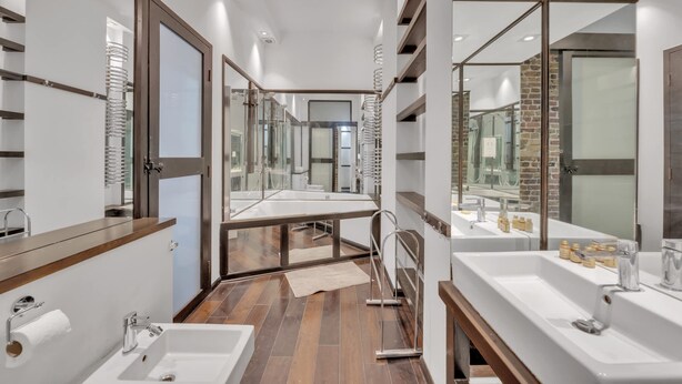 Un baño moderno con un espejo largo, dos lavamanos y piso de madera.