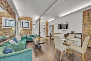 Ein modernes Wohnzimmer mit Backsteinwand, grünen Sofas, einem Glastisch und einem an der Wand befestigten Fernseher.