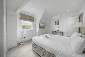 Ein Schlafzimmer mit einem Bett, einem Standventilator, einem Fenster, einem Gemälde, einem Nachttisch und einer Lampe.