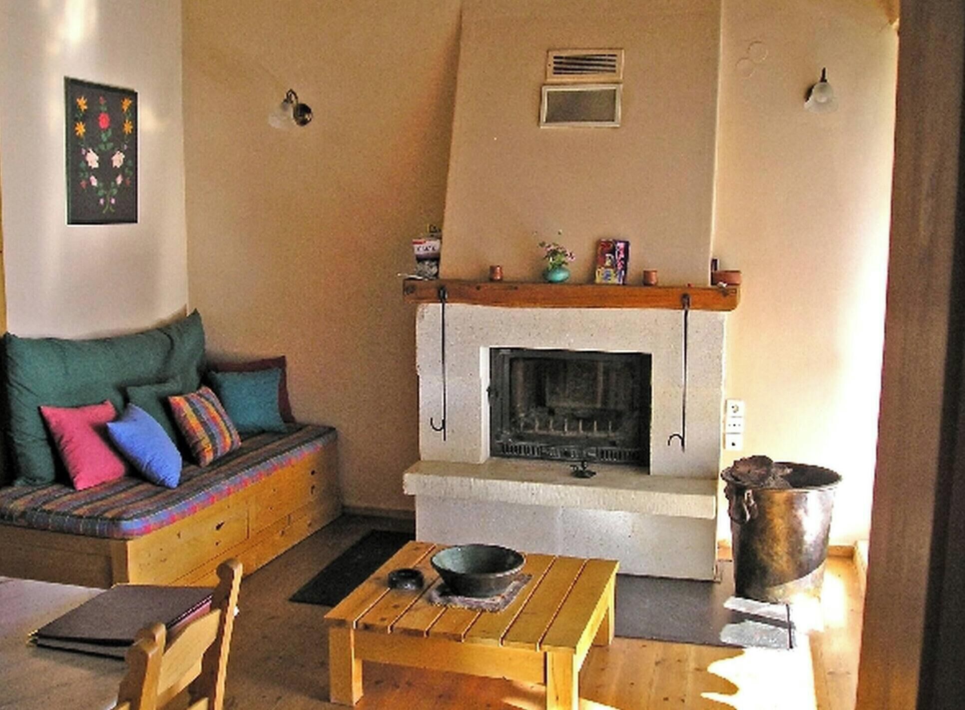 Un salon chaleureux avec une cheminée, un canapé agrémenté de coussins colorés et une table en bois sur laquelle est posé un saladier.
