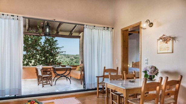 Comedor con mesa y sillas, un cuenco de fruta y vistas a un jardín a través de grandes puertas de cristal.