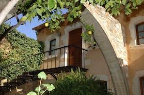 Un bâtiment en pierre doté d’un balcon, d’une fenêtre avec des volets et d’un arbre fruitier.