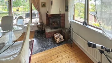 A cozy living room with a fireplace, wooden flooring, and large windows offering a view of the outdoors.