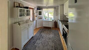 A narrow kitchen with white cabinetry, a window with lace curtains, and a patterned rug.