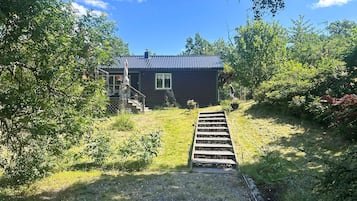 A house with a wooden staircase leading to a porch, surrounded by greenery.