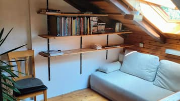 Une pièce mansardée chaleureuse avec un plancher en bois, un canapé, un fauteuil et des étagères à livres.