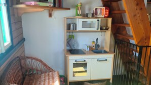 A cozy room with a wooden staircase, a wicker sofa, a blue storage bin, a white cabinet with a microwave, and a shelf with books and a toy. - A quaint, historic wooden house in the quiet mountain village of Daxstein am Brotjacklriegel (Zenting)
