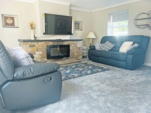 Ein Wohnzimmer mit Kamin aus Stein, einem flachbildfernseher darüber, einem blauen Sofa mit Kissen und einem grauen Fernsessel.