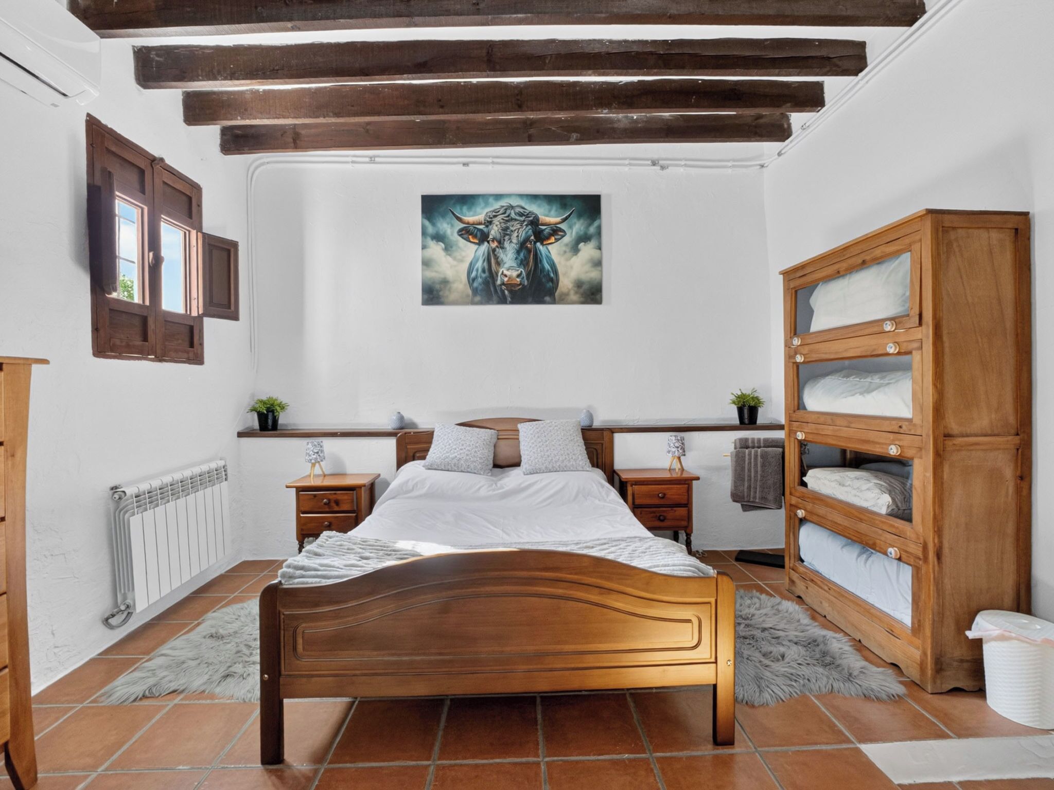 Un dormitorio con una cama de madera, un radiador, una estantería y un cuadro en la pared.