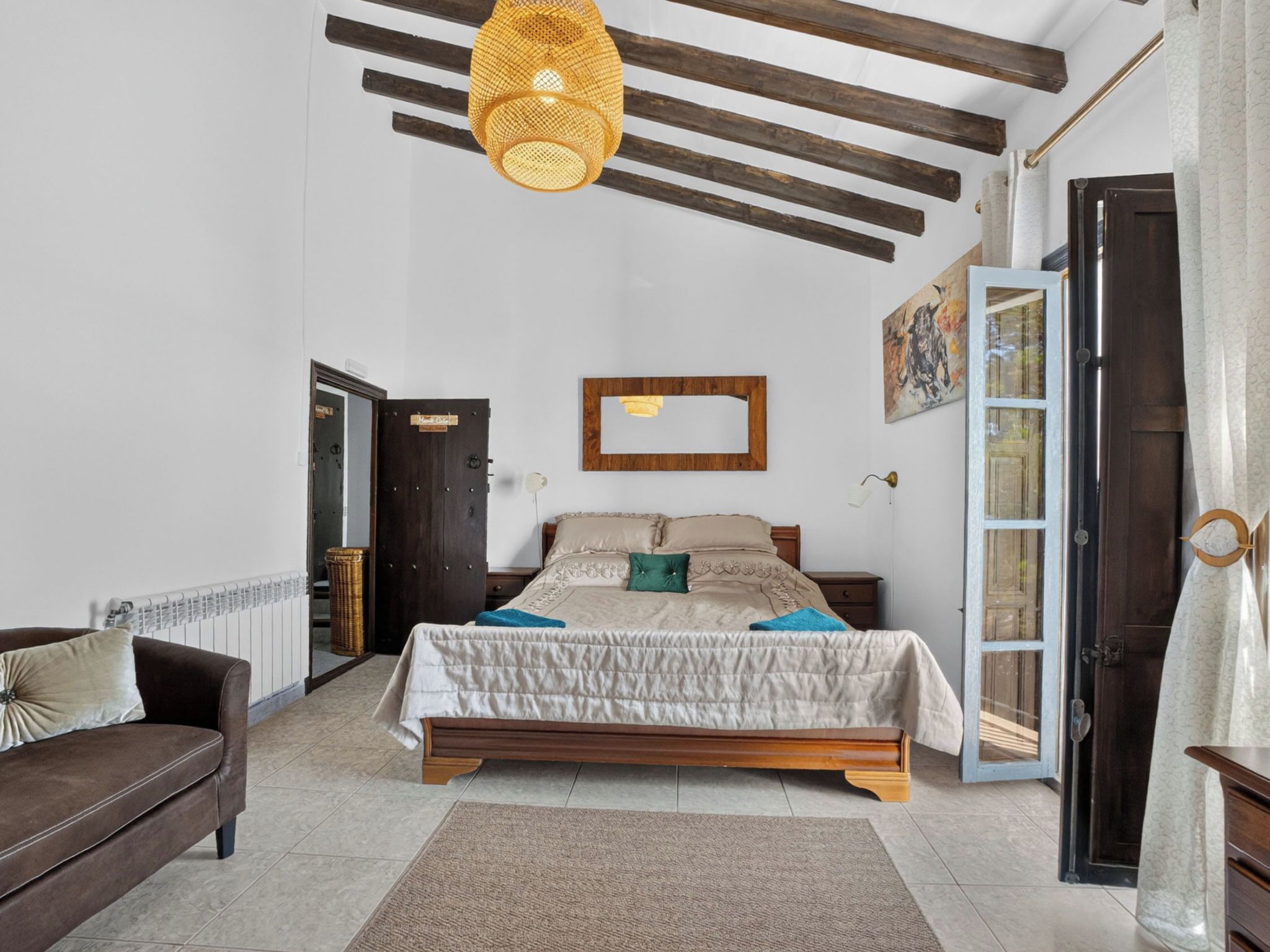 Une chambre à coucher avec un lit, une tête de lit en bois, un luminaire suspendu, une porte et une fenêtre.