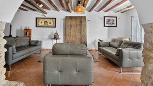 Un salón con dos sofás, una mesa de centro y una chimenea. El techo de madera tiene vigas a la vista y una lámpara colgante.