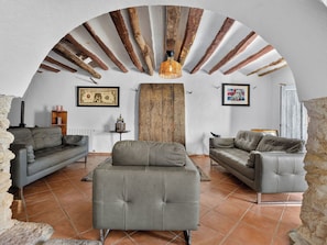 Ein Wohnzimmer mit zwei Sofas, einem Couchtisch und einem Kamin. Die Holzbalkendecke ist sichtbar und eine Hängeleuchte ist angebracht.