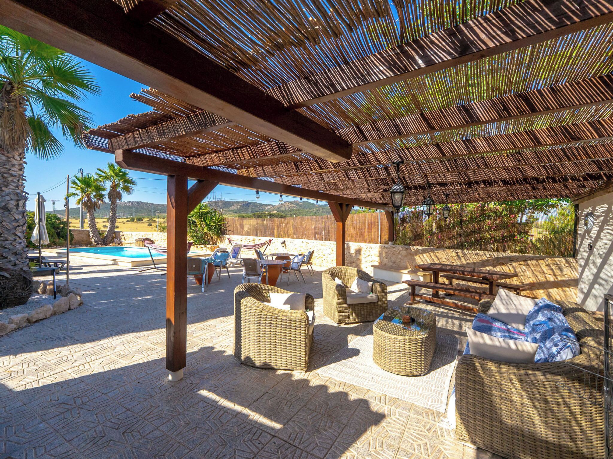 Un patio al aire libre con mobiliario de mimbre, piscina y pérgola.