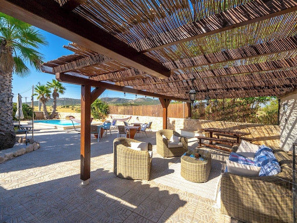An outdoor patio area with wicker furniture, a pool, and a pergola.
