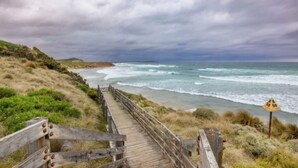 En träpromenad som leder till en strand med utsikt över havet, en skylt som visar att det är 50 meter dit, och en molnig himmel.