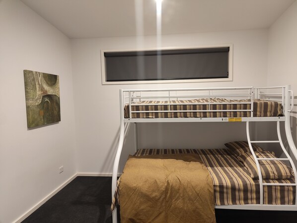 A bunk bed with a window above, a painting on the wall, and a carpeted floor.