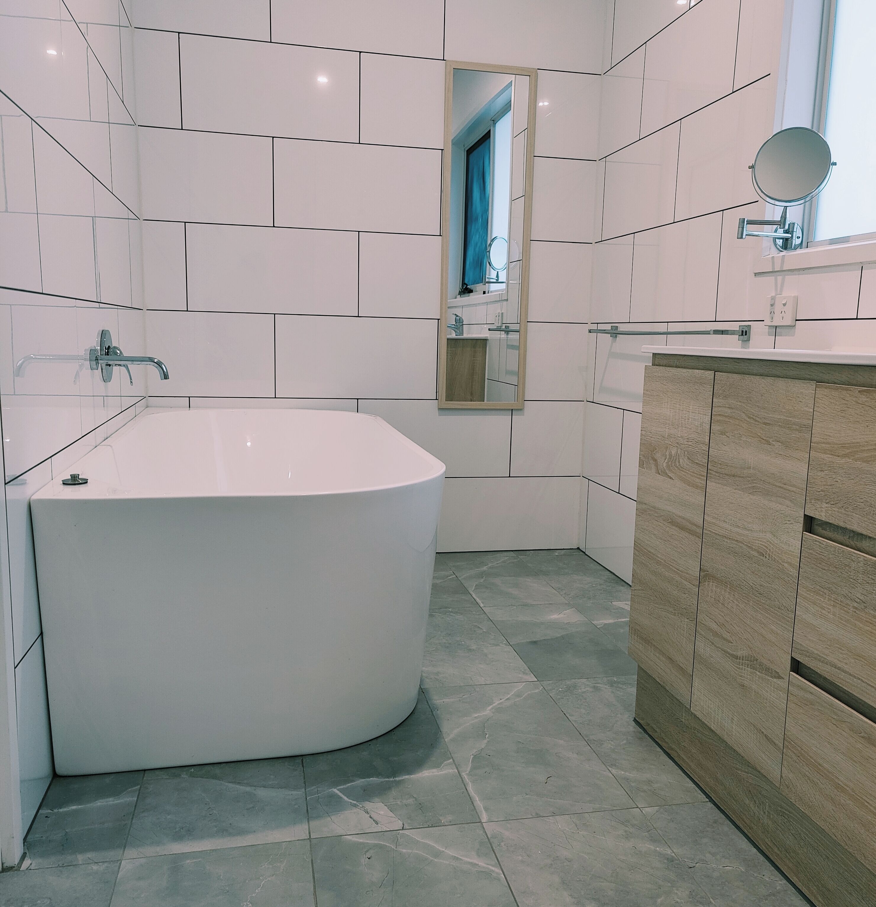 Une salle de bain moderne avec une baignoire sur pieds, un meuble-lavabo en bois et un miroir.