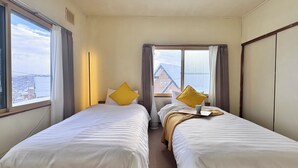 A hotel room with two beds, a window with curtains, and a view of buildings. - The Nest Furano (Furano)