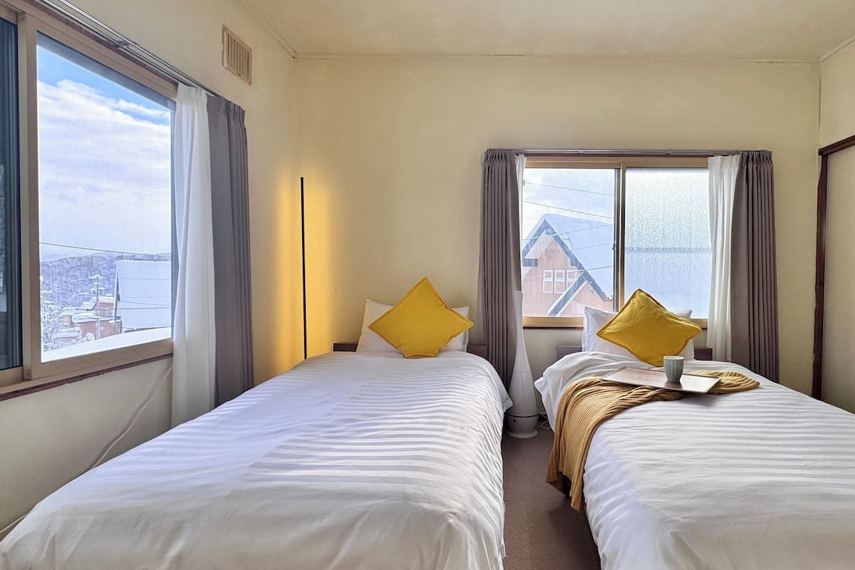 A hotel room with two beds, a window with curtains, and a view of buildings.
