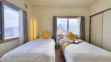 A hotel room with two beds, a window with curtains, and a view of buildings.