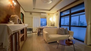 A cozy room with a sofa, a small table, a window with curtains, and a wooden cabinet. - The Nest Furano (Furano)