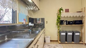 A kitchen with stainless steel appliances, a sink, and a window with a view of cherry blossoms. - The Nest Furano (Furano)
