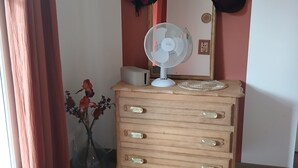 A room with a wooden dresser, a mirror, and a fan. There are hats hanging on the wall above the dresser.