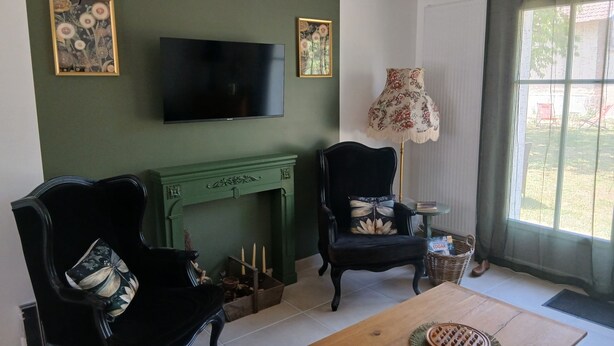 A living room with a fireplace, two armchairs, a television, and a window with a view.