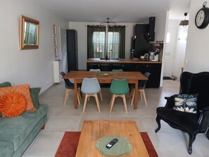 A modern living room with a dining area, a sofa, a coffee table, and a black armchair.