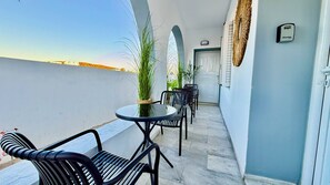 Un balcon avec une table ronde et des chaises, des plantes en pot et une porte dotée d’un dispositif de sécurité.