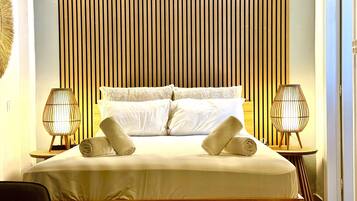 A neatly made bed with pillows and rolled towels, two bedside lamps, and a wooden slat headboard.