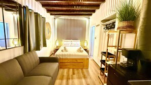 Ein Zimmer mit einem Bett, einem Sofa, Holzboden, einem Fernseher und einer Pflanze.