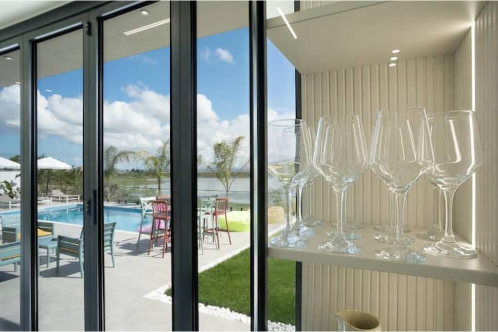 A modern interior with a pool view, clear glassware on a shelf, and a white wall.