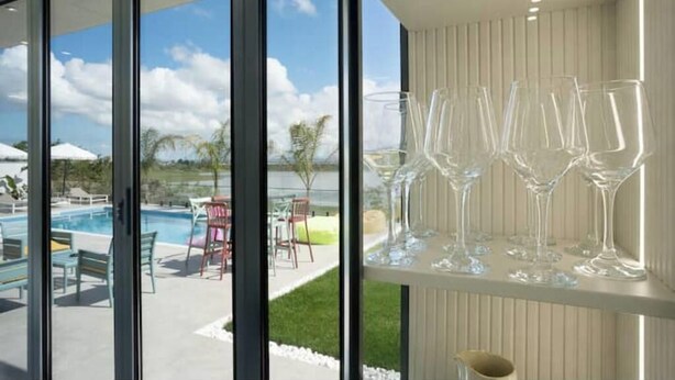 Ein modernes Interieur mit Blick auf einen Pool, klares Glasbesteck auf einem Regal und einer weißen Wand.