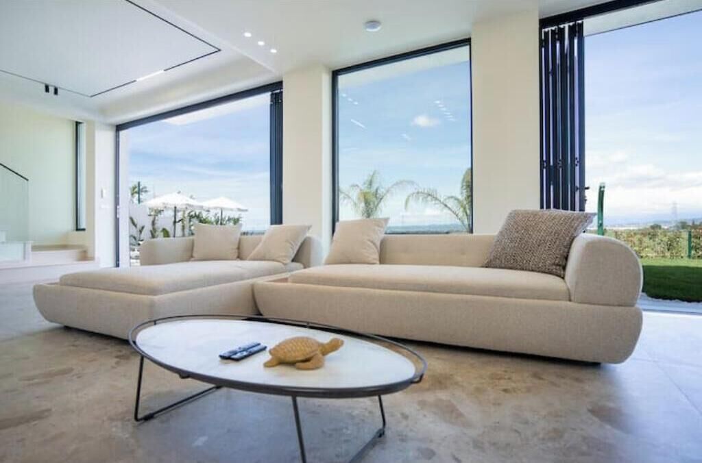 A modern living room with a sectional sofa, a round coffee table, and a large window offering a view of the outdoors.