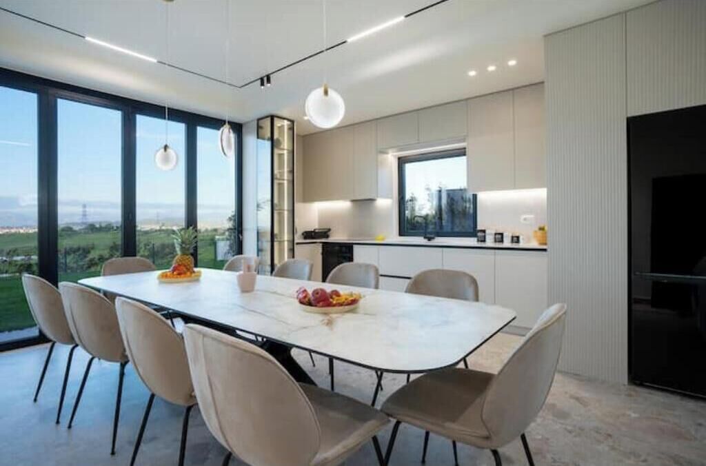 A modern kitchen with a large island, a dining area with a table and chairs, and a view of the outdoors.