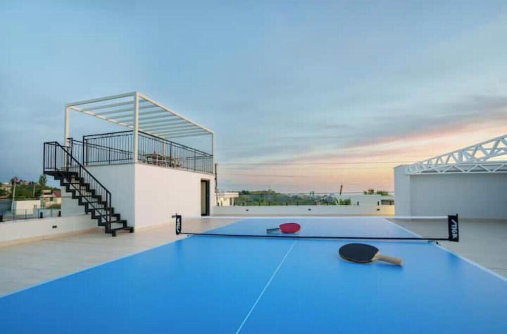 Uma quadra de tênis no terraço, com rede, uma raquete de ping pong e uma escadaria para um andar superior.