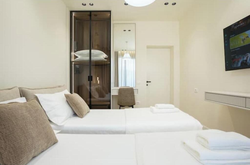Une chambre d’hôtel avec deux lits, une armoire, un bureau et un téléviseur fixé au mur.