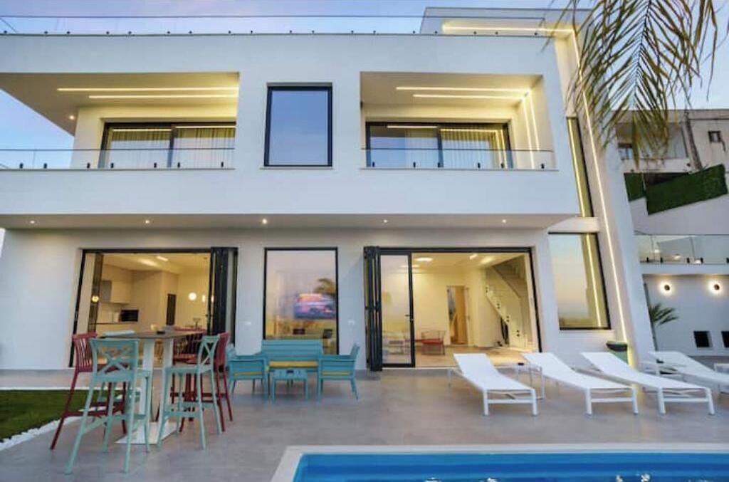 A modern two-story building with a swimming pool, outdoor seating, and a balcony.