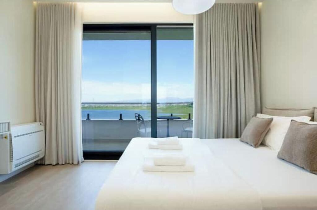 A hotel room with a large bed, a view of the sea, and a sliding glass door.